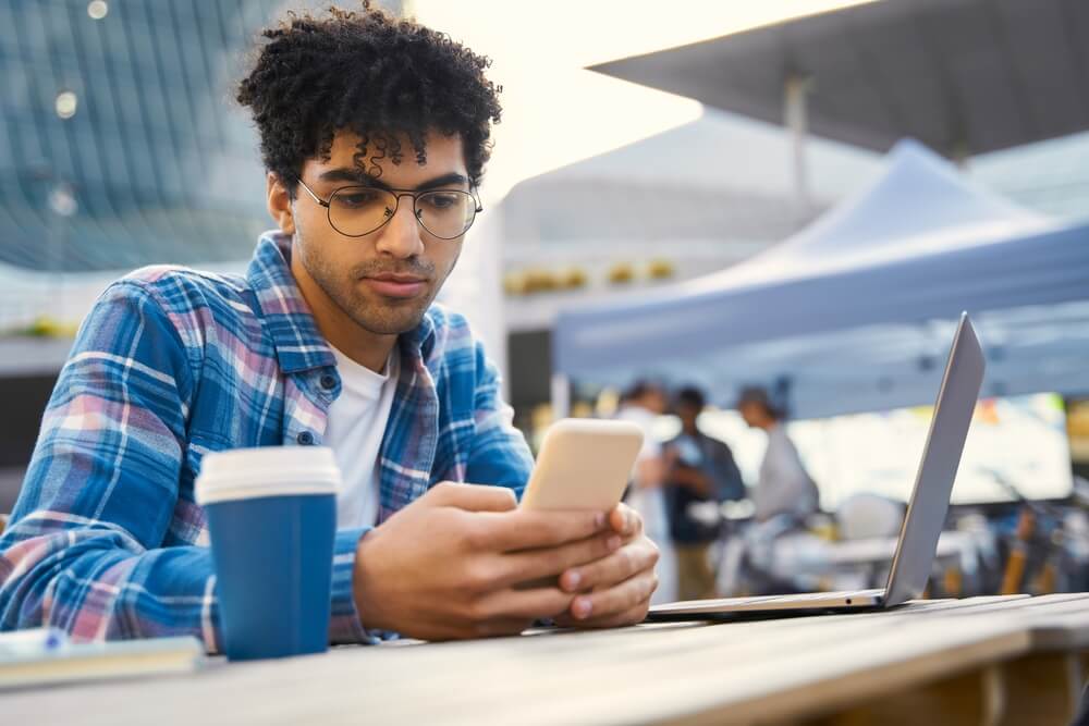 Young man using a smartphone beside his laptop, illustrating mobile internet usage and digital connectivity